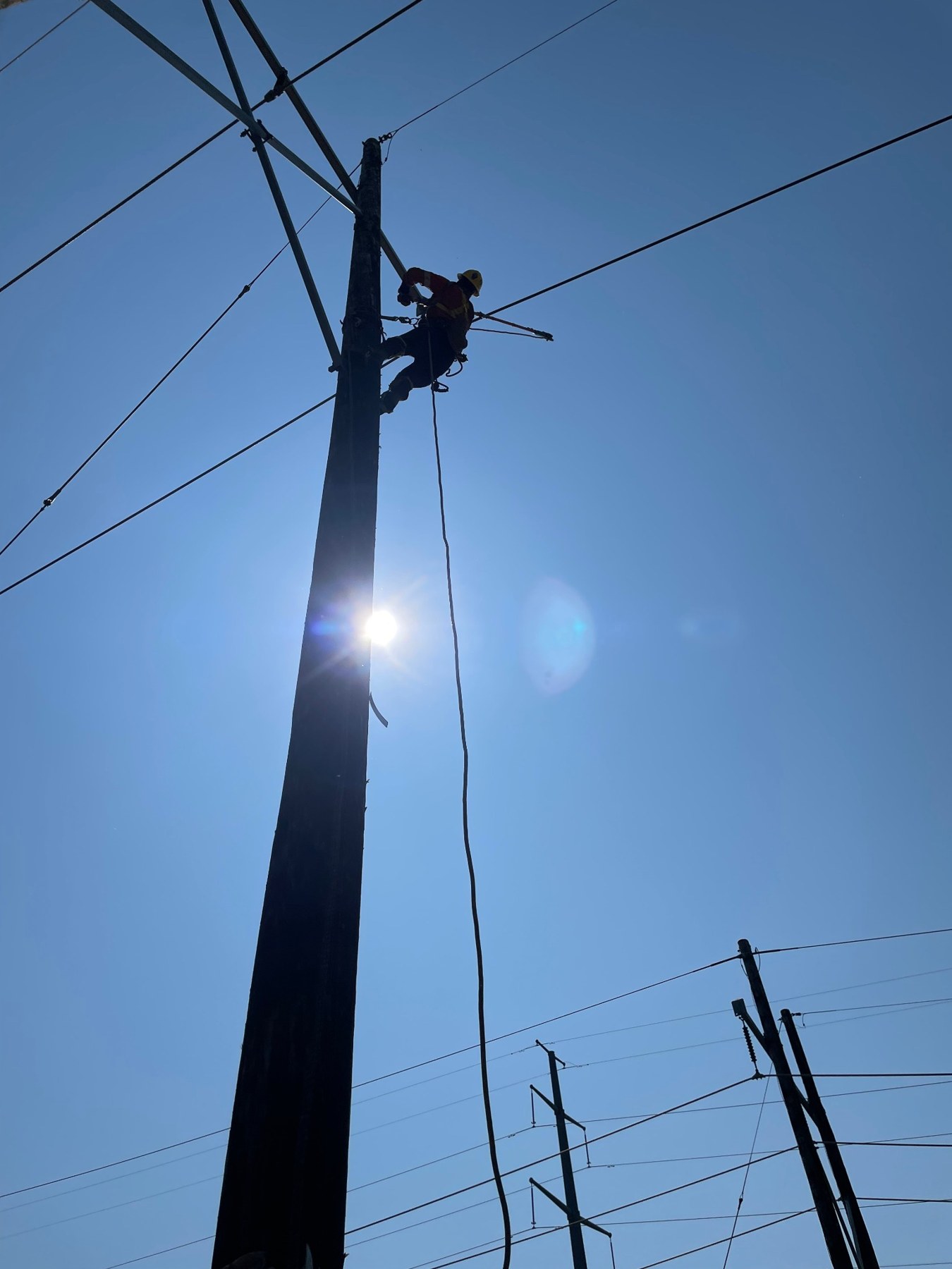 Powerline worker aloft against a clear blue sky